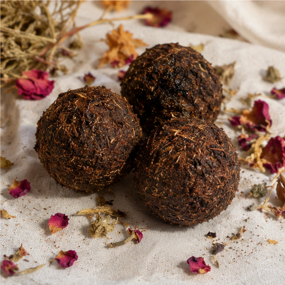 Trois boules d’encens artisanales aux plantes, mises en scène sur tissu naturel avec fleurs séchées.