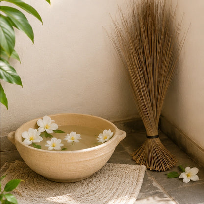 Balai traditionnel africain près d’un bol d’eau rituelle fleuri, pour évoquer purification et protection du foyer