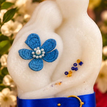 Gros plan sur la bougie Couple en cire blanche : fleur bleue perlée, perles dorées et ruban satiné évoquant l'union.
