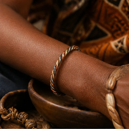 Bracelet trois métaux porté au poignet dans une scène naturelle inspirée des traditions spirituelles africaines.