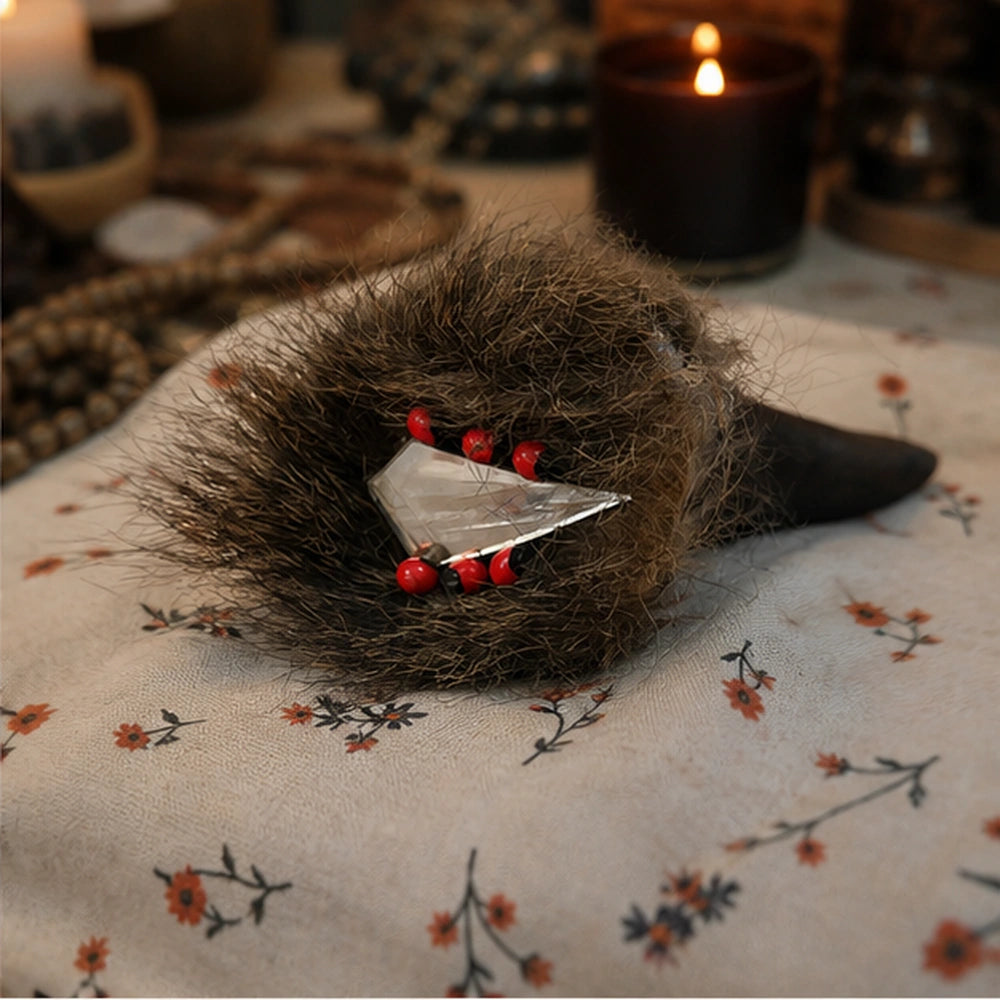Corne rituelle avec graines sonores, perles rouges et cristal, posée sur un tissu fleuri dans une ambiance de rituel spirituel