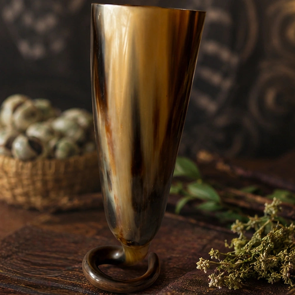Détail de la coupe rituelle en corne sur table en bois avec herbes, cauris et ambiance de purification.