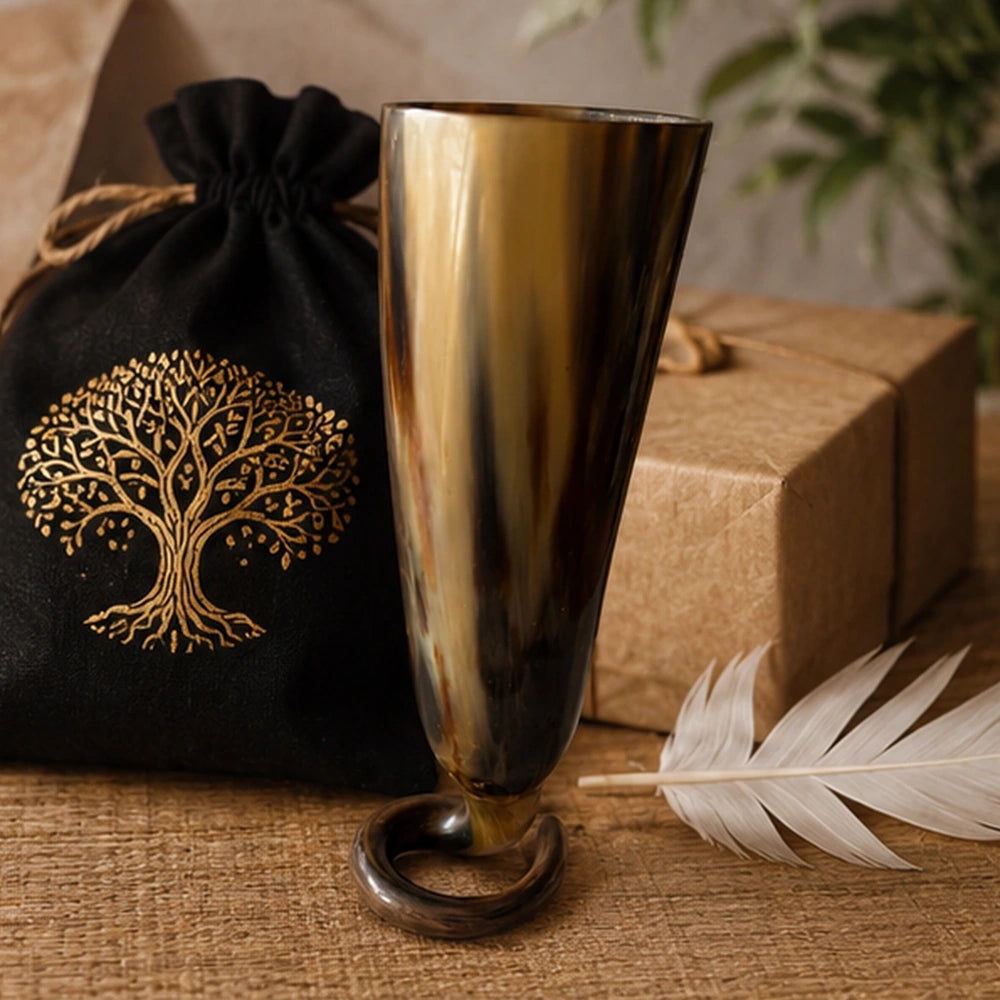 Coupe rituelle en corne mise en scène avec pochon, plume et coffret dans une ambiance premium d’autel.