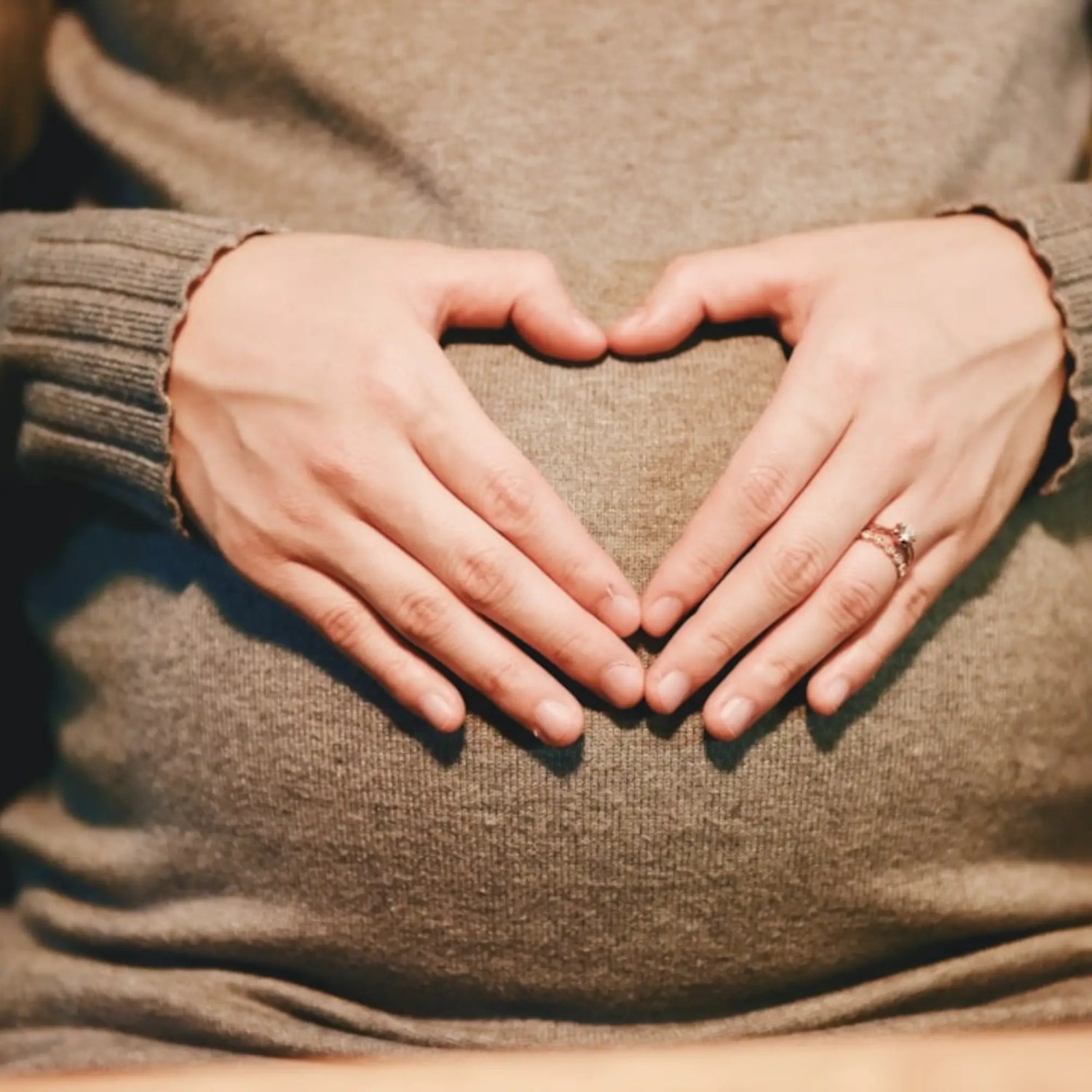 Une femme enceinte qui a disposé ses mains en forme de cœur sur son ventre