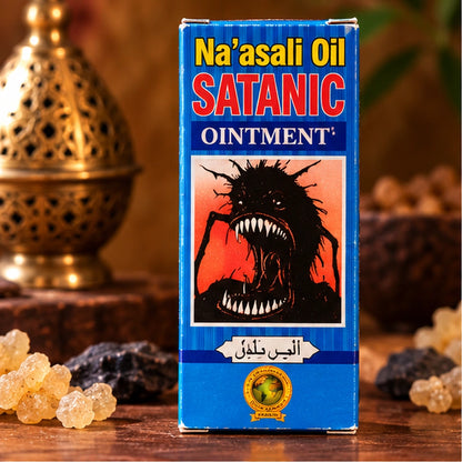 Boîte bleue Na’asali Oil Satanic Ointment de face, posée sur une table en bois parmi des résines et une lanterne dorée.