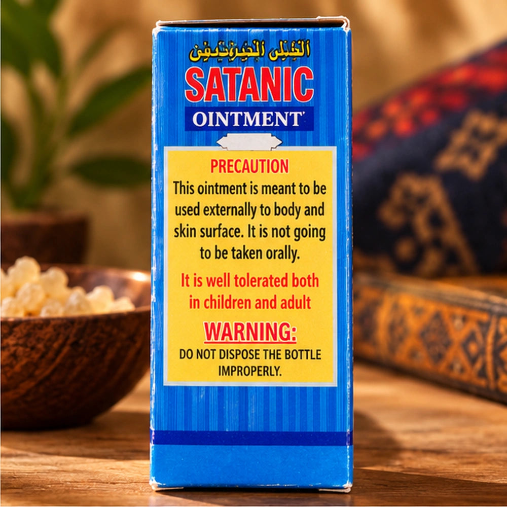 Dos de la boîte bleue Satanic Ointment, avec étiquette jaune de précautions, près de résines et de tissus décoratifs.