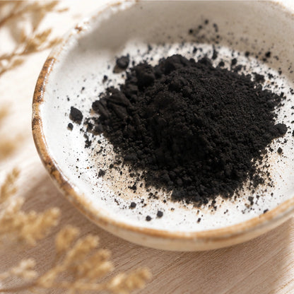 Gros plan sur la poudre noire des Cendres Sacrées dans une coupelle artisanale, pour rituel de purification.